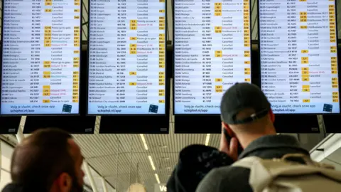 Reuters People look at departures screens showing delayed and cancelled flights at Amsterdam Airport Schiphol,