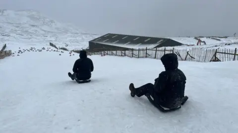 Glencoe Moutain resort Two people wearing black jackets sledding down a snow covered hill