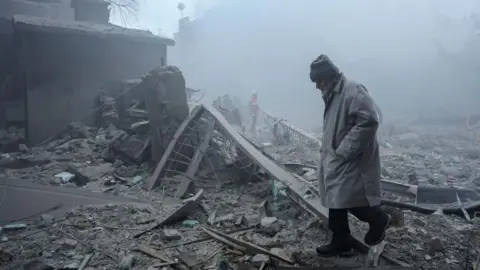 EPA/Shutterstock A man walks among the rubble after a Russian strike on a residential area in the city of Kharkiv, north-eastern Ukraine. Photo: 2 January 2026