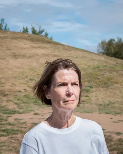 Sandi Partridge in a white t-shirt, looking away from the camera, in a park near her home.
