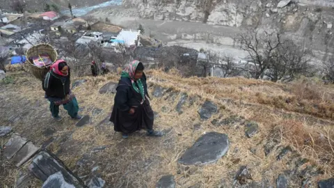 Getty Images In this picture taken on February 10, 2021, women from Raini Chak Lata village walk along a mountain path in Chamoli district. - Long before this month's deadly flash flood in a remote Indian Himalayan valley, Kundan Singh Rana knew that all the construction work in the fragile region would one day mean disaster.