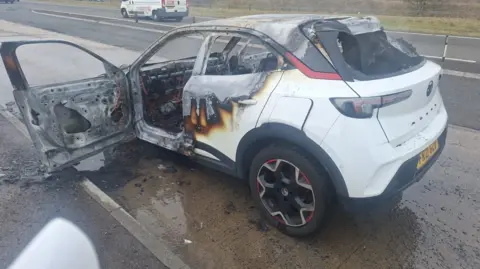 Anne Marie Thomas A side view of the white car completely damaged by the fire. All the windows have gone and there is debris around the vehicle. 