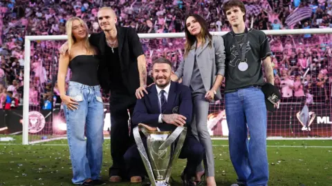 Getty Images Sir David Beckham, co-owner of Inter Miami CF, and Victoria Beckham pose with the trophy with Cruz Beckham, Romeo Beckham after winning the Championship following the Audi 2025 MLS Cup Final match between Inter Miami CF and Vancouver Whitecaps FC at Chase Stadium on December 06, 2025 in Fort Lauderdale, Florida