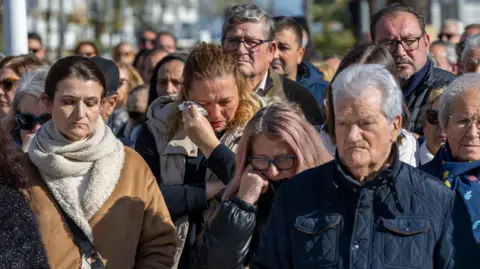 EPA People gather to observe a minute of silence in memory of the victims of the train collision that occurred on 18 January, in Punta Umbria, Huelva, Spain, on 20 January 2026. Several residents of Punta Umbria are among those killed after a high-speed train carrying more than 300 passengers derailed and collided with an oncoming train on an adjacent track. Emergency services remain at the scene as recovery efforts continue.