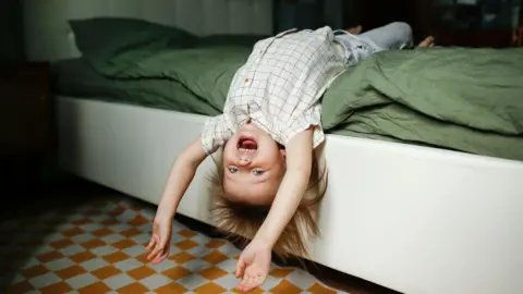 Getty Images A young child smiling, while hanging upside down from the bed