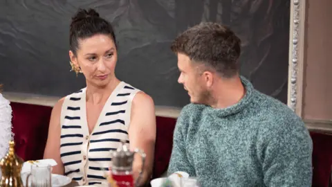 Studio Lambert/Euan Cherry/PA Rachel Duffy and Matthew Hyndman sitting beside each other at a table. Rachel, on the left, is wearing a white top with navy stripes and no sleeves. Her dark brown hair is tied up. Matthew, with short brown hair, is wearing a blue wooly jumper. 