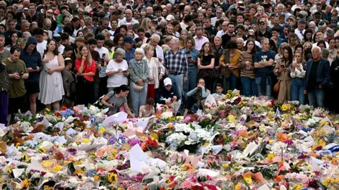 Getty Images Mourners gather in front of a sea of floral tributes at a makeshift memorial at the Bondi Pavilion in memory of the victims of a shooting at Bondi Beach