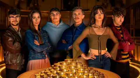 The six finalists stand behind a table with a pile of gold coins