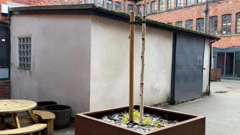 supplied A small concrete hut with a large black door and tin roof