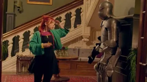 Jessie saluting the suit of armour on her way out of the castle at night