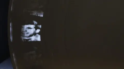 A flickery image of the device in action with a mans face visible in the light