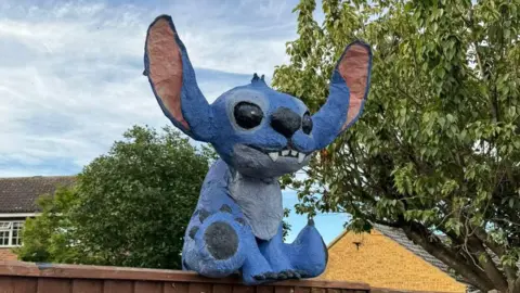 Matt Jerome An effigy of Disney character Stitch sitting on a garden fence.