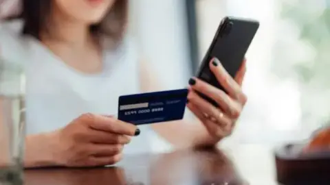 Getty Images Stock image of female hands holding a credit card and looking at a phone
