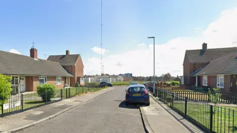 Google Egglescliffe Close has a row of terraced bungalows with a black fence in front of them. A sign attached to the fence reads "Egglescliffe Close". It is a Google Maps screenshot.