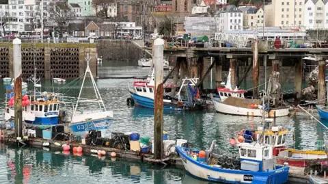 Matt Judge/BBC Fish Quay St Peter Port is filled with small fishing boats moored at pontoons in the harbour. Houses are close to the the harbourside.
