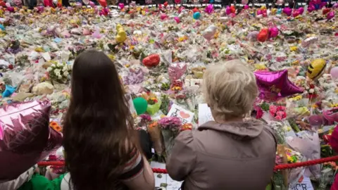 AFP via Getty Images Two women stand in front of tributes to the victims of the Manchester Arena bombing in 2017