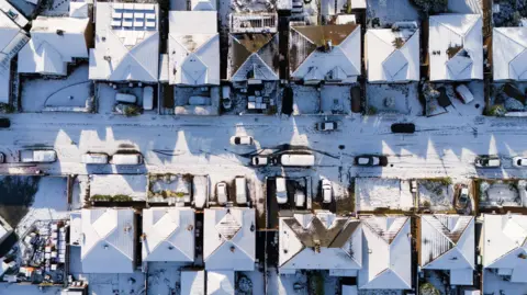 PA Media aerial view showing the tops of snow-clad roofs on houses and cars lining a street