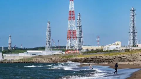 Getty Images Two people walking on a beach, with the Kashiwazaki-Kariwa nuclear power plant in the background.