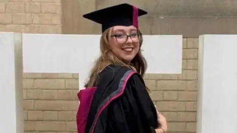 Nottinghamshire Police Stephanie Irons wearing a graduation gown and cap in front of a sign for Nottingham Trent University
