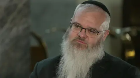 BBC Rabbi Daniel Walker. He is wearing a Kipa, glasses, and has a long grey beard. 
