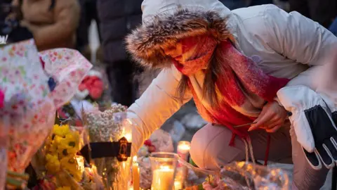 Getty Images A woman in a heavy winter coat places an object at a candle-lit vigil for Alex Pretti.