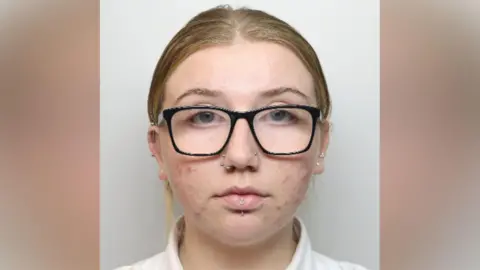 Northamptonshire Police A woman with black-framed glasses, two nose piercings and a lip piercing looks at the camera.