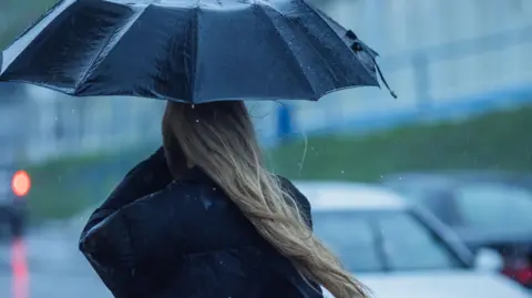 Getty Images A woman with long hair is pictured in an anonymous, blurred road, holding up an umbrella in torrential rain
