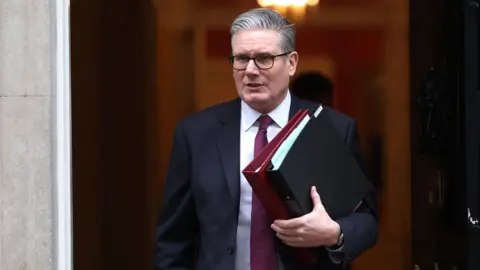 EPA Starmer looks away from camera as he exits Downing Street holding files while wearing a suit and tie before PMQs on Wednesday.