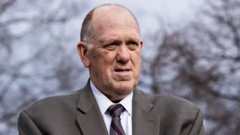 EPA Tom Homan stands outside in front of leafless trees wearing a grey suit.