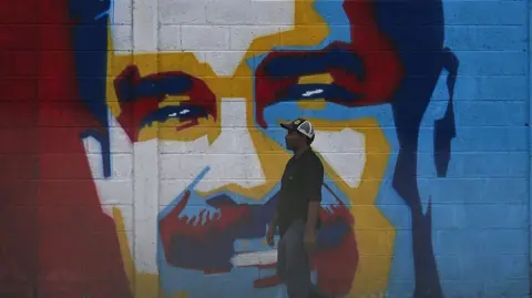 Getty Images A man walks past a graffiti depicting Venezuelan President Nicolas Maduro in Caracas on January 3, 2026. The colours used in the graffiti are yellow, blue, red and white. 