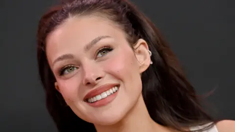 Getty Images Nicola Peltz smiling, she has her long red/brown hair down.